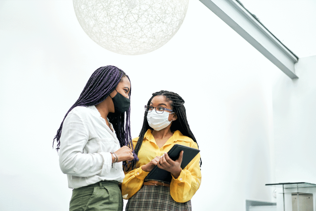 Two woman in masks talking to each other.