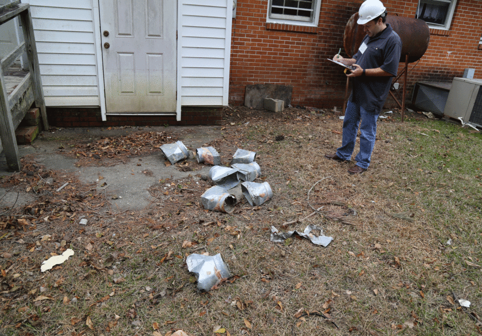 Man with a hard hat looking at broken pieces of metal on ground